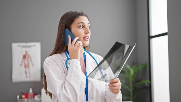 Fiatal gyönyörű spanyol nő orvos keres röntgen beszél okostelefon a klinikán - Fotó, kép