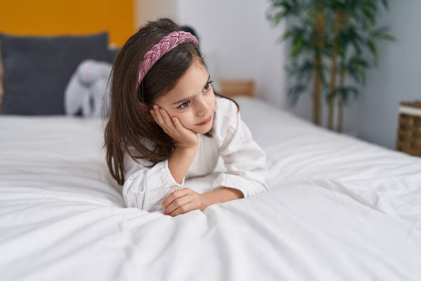 Adorable chica hispana acostada en la cama con expresión triste en el dormitorio - Foto, Imagen