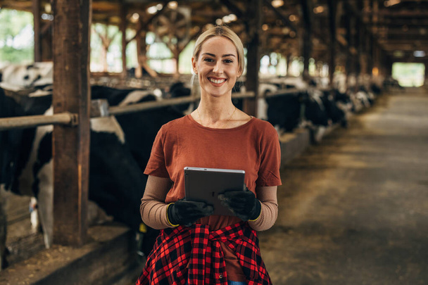 Portrait of a pretty farm girl standing in a stable with a digital tablet. - Foto, imagen