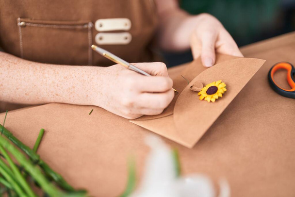 Nuori punapää nainen kukkakauppa kirjallisesti kirjekuoressa klo kukkakauppa - Valokuva, kuva