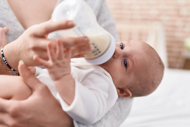 Adorable caucasian baby sucking feeding bottle at bedroom - Foto, afbeelding
