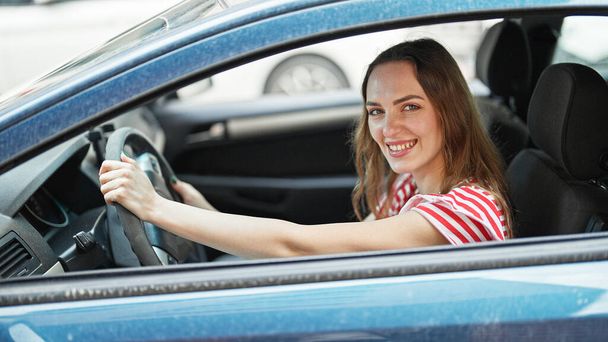 Mujer rubia joven conduciendo un coche sonriendo en la calle - Foto, Imagen