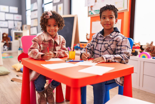 Schattige Afrikaanse Amerikaanse jongen en meisje kleuters zitten op tafel tekenen op papier op de kleuterschool - Foto, afbeelding