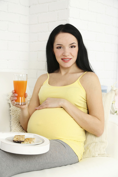Young pregnant woman relaxing on sofa with glass of juice on home interior background - Foto, Imagem
