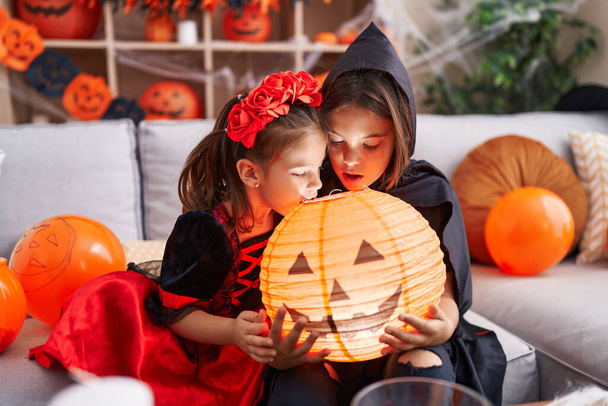 Adorable niño y niña con disfraz de halloween mirando en lámpara de calabaza en casa - Foto, imagen