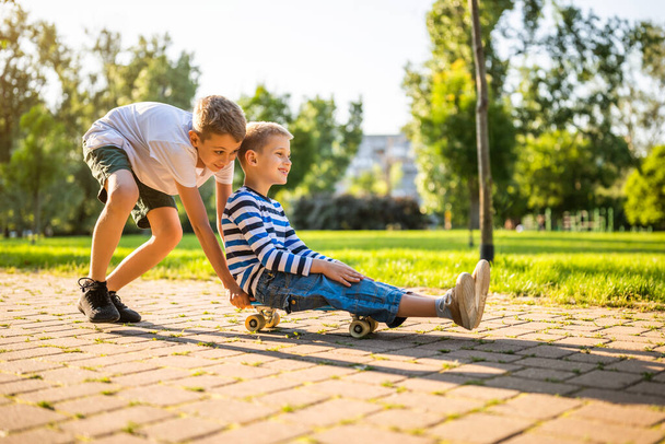 Two boys are having fun with skateboard in park. Playful children in park, happy childhood. - Fotoğraf, Görsel