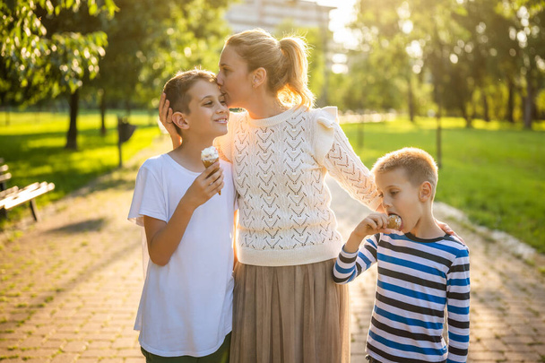 Портрет щасливої матері-одиначки з двома синами в парку в сонячний день. Хлопці їдять морозиво
. - Фото, зображення