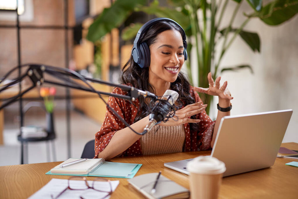Beautiful radio host recording podcast in studio. Young mixed race woman recording a podcast in studio. Smiling multiethnic woman speaking on microphone over laptop at her home studio. - Zdjęcie, obraz