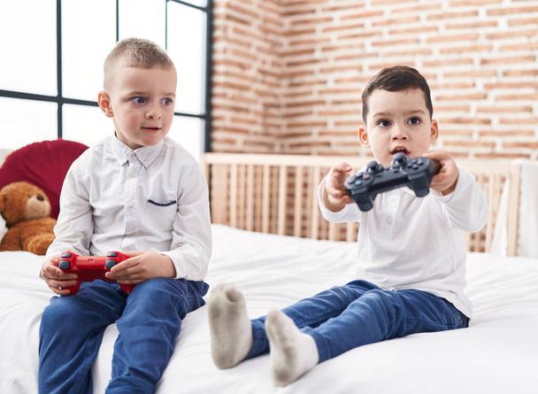 Adorable boys playing video game sitting on bed at bedroom - Photo, Image