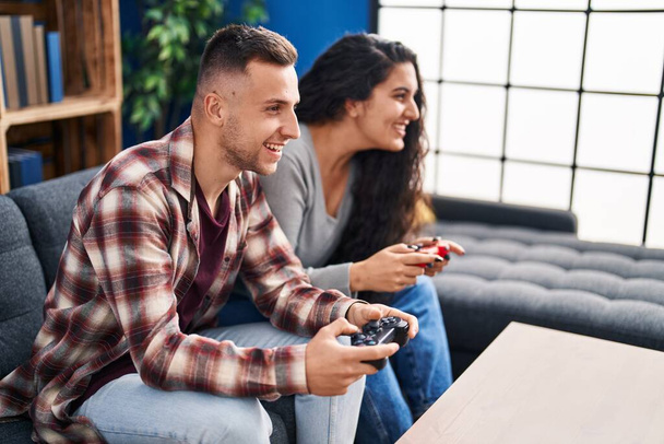 Мужчина и женщина играют в видеоигры, сидя дома на диване - Фото, изображение