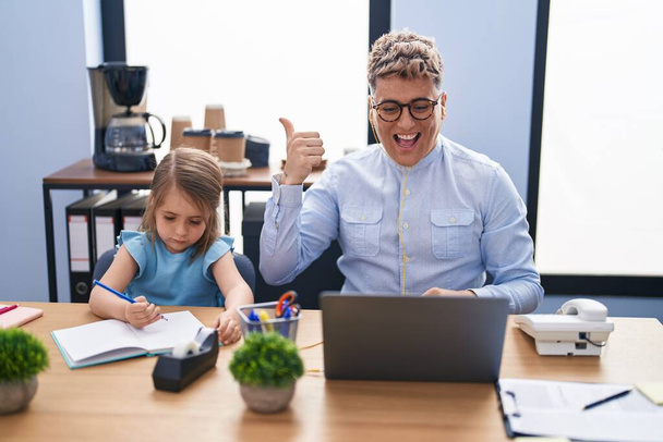 Mladý otec a dcera pracují společně v kanceláři a ukazují palcem nahoru na stranu, usmívají se šťastně s otevřenými ústy  - Fotografie, Obrázek