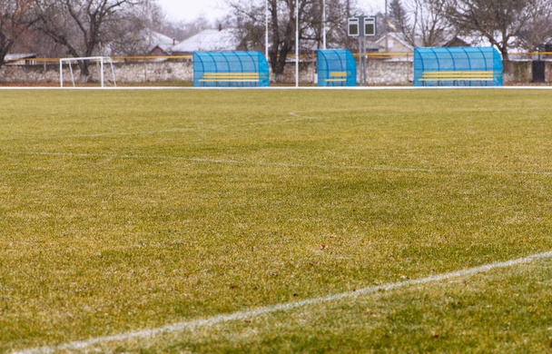 Άποψη ενός άδειου γηπέδου ποδοσφαίρου καλυμμένου με γρασίδι με πύλες και στέκεται για τους θεατές, το χειμώνα κατά τη διάρκεια της ψυχρής περιόδου - Φωτογραφία, εικόνα