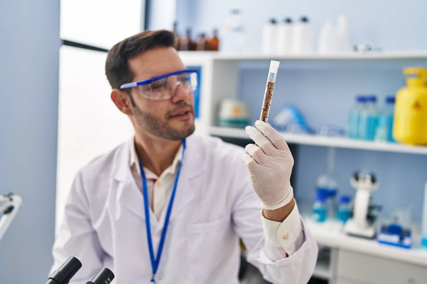 Young hispanic man scientist holding test tube at laboratory - Φωτογραφία, εικόνα