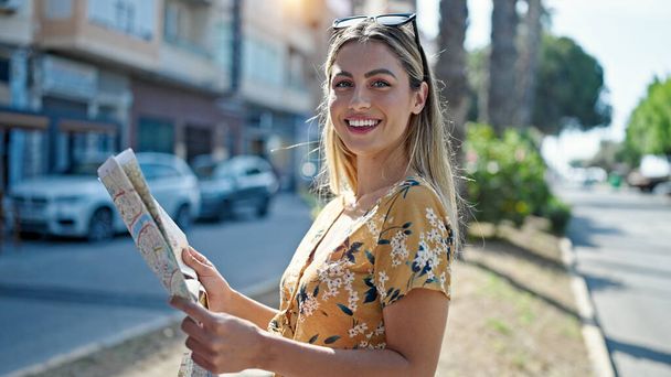 Junge blonde Touristin lächelt selbstbewusst und sieht Stadtplan auf Straße - Foto, Bild