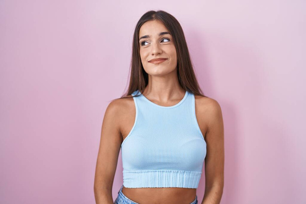 Young brunette woman standing over pink background smiling looking to the side and staring away thinking.  - Foto, imagen