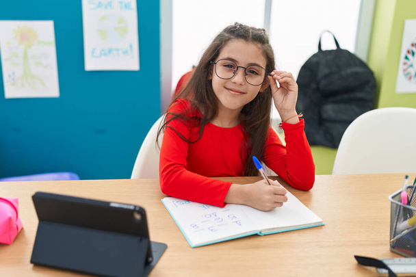 Entzückende hispanische Studentin schreibt mit Touchpad im Klassenzimmer auf Notizbuch - Foto, Bild