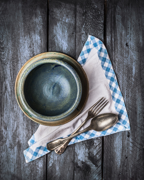 Empty bowl, spoon and fork with napkin on dark wooden background, top view - Fotó, kép