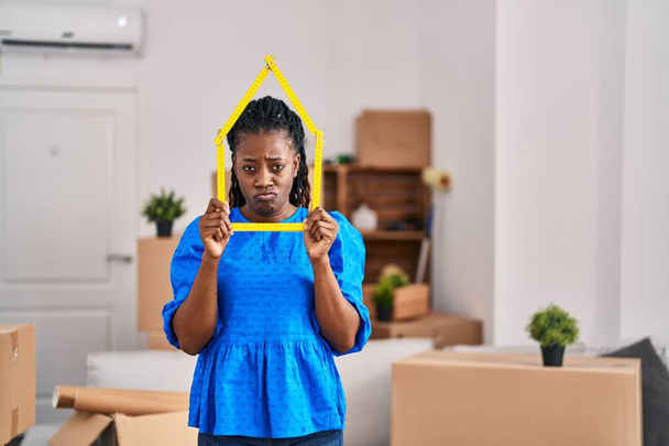 African woman with braided hair at new home holding ruler skeptic and nervous, frowning upset because of problem. negative person.  - Photo, image