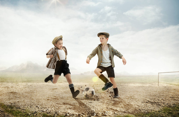 Active little boys, children in retro style clothes playing football outdoors on a daytime. warm sunny day on countryside. Concept of sport, childhood, retro style, active lifestyle, summer vacation - Фото, зображення