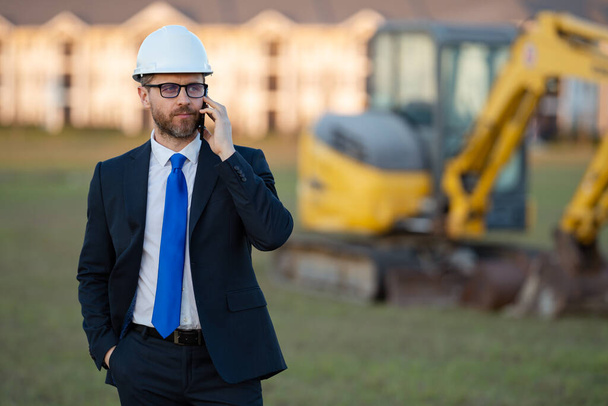 Architect at a construction site. Architect man in suit and helmet at construction site. Confident architect standing at construction. Investor or civil engineer. Outdoor portrait of hispanic - Foto, afbeelding