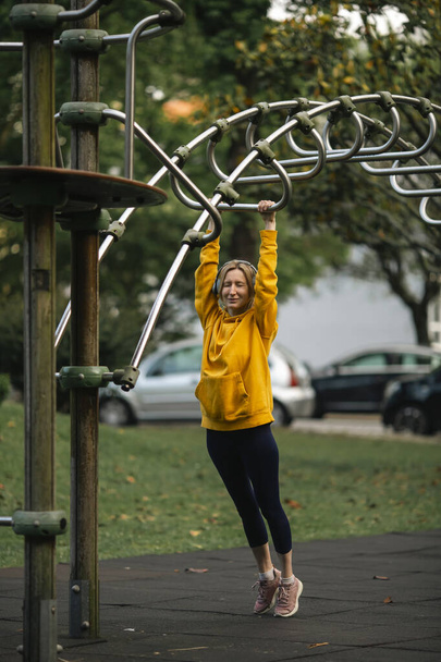 A woman wearing headphones exercising outdoors in an outdoor playground. - Fotó, kép