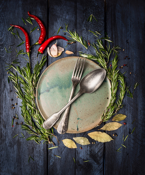 Spoon and Fork on plate with herbs and spices frame on dark blue wooden table, top view - Photo, Image