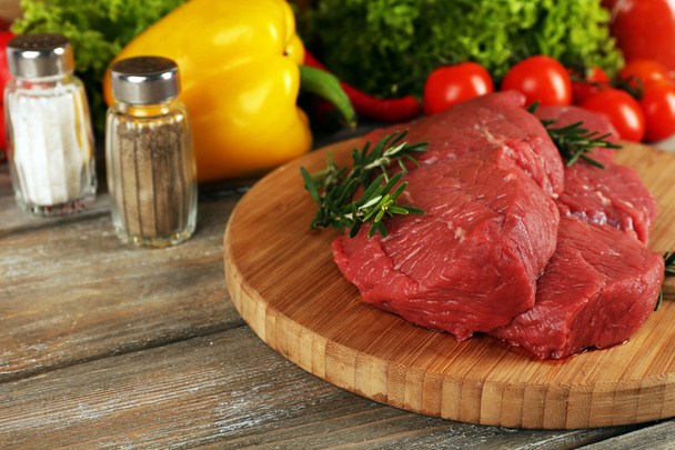 Raw beef steak on cutting board with vegetables and spices on wooden background - Photo, image