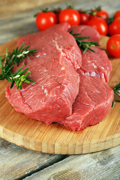 Raw beef steak with rosemary and cherry tomatoes on cutting board on wooden background - Foto, imagen