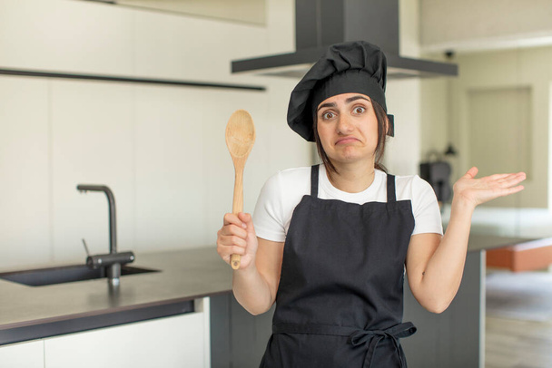 young woman shrugging, feeling confused and uncertain. chef concept - Foto, Imagen