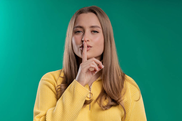 Smiling woman holding finger on lips, blue studio background. Pretty lady with gesture of shhh, secret, silence, conspiracy, gossip concept. High quality - Photo, image
