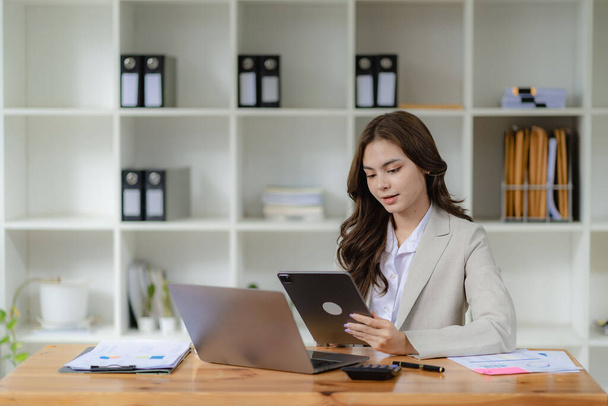 Young female accountant, company worker working with laptop and accounting documents checking financial data or marketing reports working in office - Foto, imagen