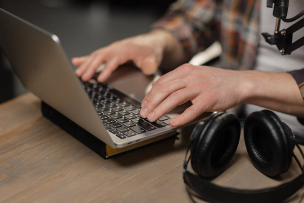 Cropped view of a man who works behind a laptop. A man in a plaid shirt is sitting at a table and typing on a laptop keyboard. High quality photo - Photo, Image