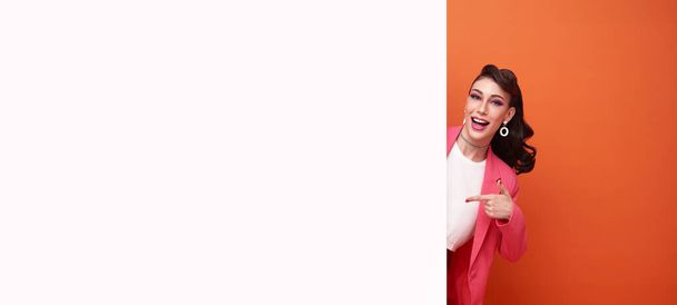 Happy smiling business woman in pink blazer hand pointing finger blank announcement banner isolated on copy space orange background. - Photo, Image