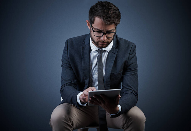 Использовать технологии, чтобы преуспеть. Студийный снимок красивого молодого бизнесмена с планшетом, сидящего на стуле на тёмном фоне - Фото, изображение