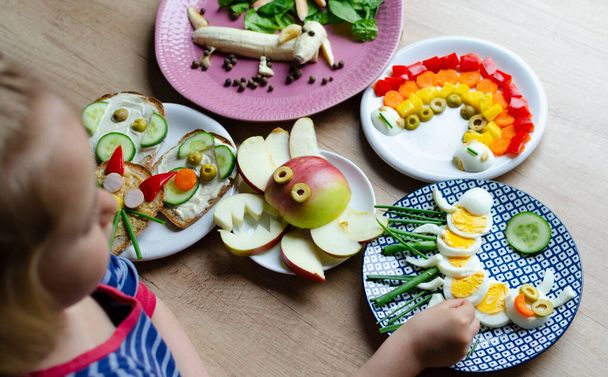 Little girl eating colorful meal and healthy vegetables and fruits in different shape. Fun with food for child in the morning. Funny breakfast for kids. - Fotoğraf, Görsel