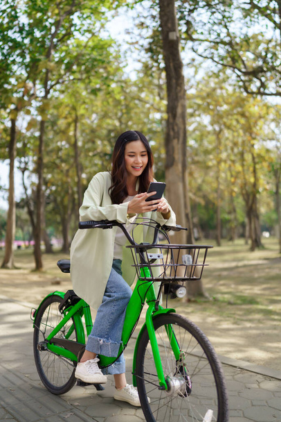 Kobiety korzystające ze smartfona do czatowania i surfowania w mediach społecznościowych po jeździe na rowerze na ćwiczenia w parku. - Zdjęcie, obraz