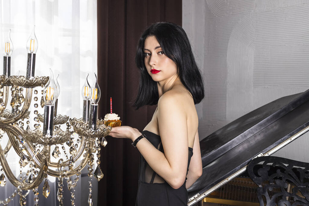 Menina bonita elegante vestida com cabelo preto e vestido comemorando 18 anos, posando contra o piano - Foto, Imagem