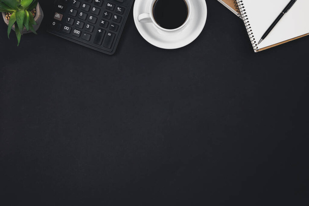 Una taza de café, bloc de notas, una calculadora y una maceta sobre un fondo negro, vista superior, espacio para copiar. - Foto, imagen