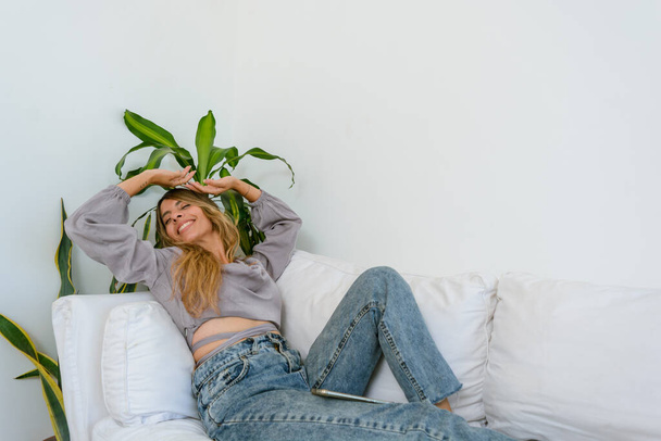 mujer latina feliz acostada en un sofá blanco vistiéndose y sonriendo, concepto de estilo de vida, espacio para copiar. - Foto, imagen