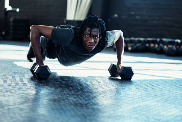 My fitness can only get better if I keep going. a young man doing push ups with dumbbells in a gym - 写真・画像