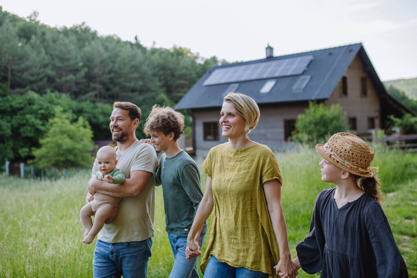 Happy family near their house with a solar panels. Alternative energy, saving resources and sustainable lifestyle concept. - Foto, afbeelding