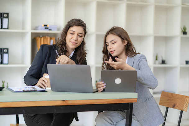 Businesswoman and accountant talking with laptop and tablet Two attractive millennial caucasian businesswoman planning project together at table in office - Photo, Image