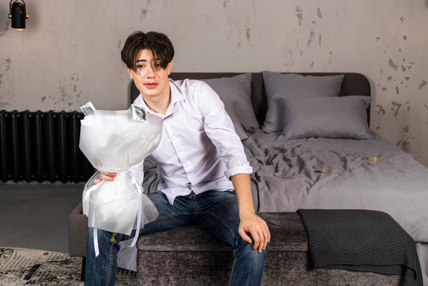 Młody mężczyzna na łóżku ze środkami antykoncepcyjnymi i bukietem kwiatów - Zdjęcie, obraz