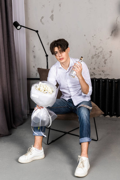 Young handsome drunk man with contraceptives bouquet of flowers, and a bottle of alcohol - Photo, Image