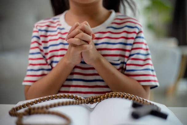 Christelijk concept. Klein Aziatisch meisje bidt dat het kruis achterhoudt. Concepten van hoop, geloof, christendom, religie,  - Foto, afbeelding