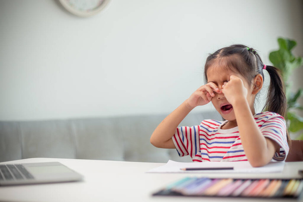 アジアの子供は家でオンラインで勉強している間にあくびをして退屈しています. - 写真・画像