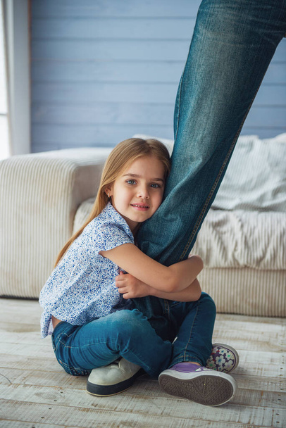 Cropped image of cute little girl looking at camera and smiling while hugging her father's leg not letting him go - Photo, Image
