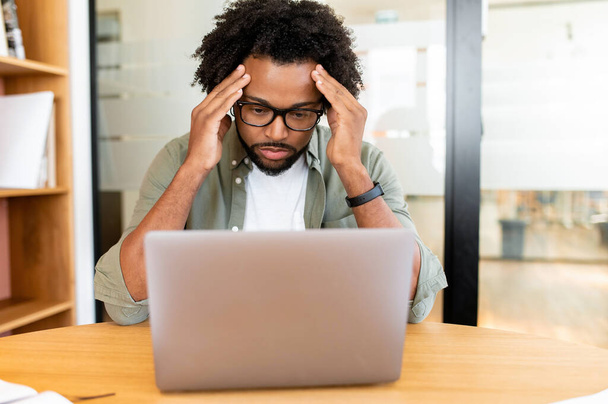 Worried african-american male employee colleague staring at laptop screen sitting on the workplace, pensive concerned businessman has problem with project, lack of new ideas - Foto, Imagen