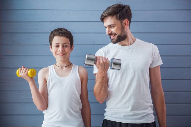 Handsome young father and his teenage son are looking at camera and smiling while working out with dumbbells - Photo, Image