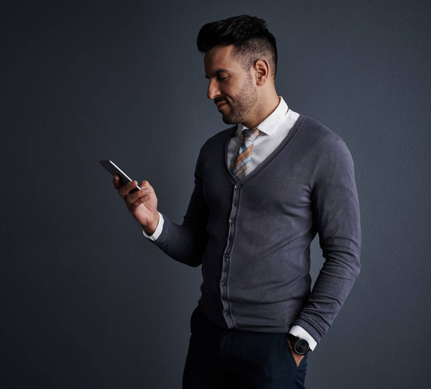 The instant way to stay in touch. Studio shot of a stylish young businessman using a mobile phone against a gray background - Photo, Image